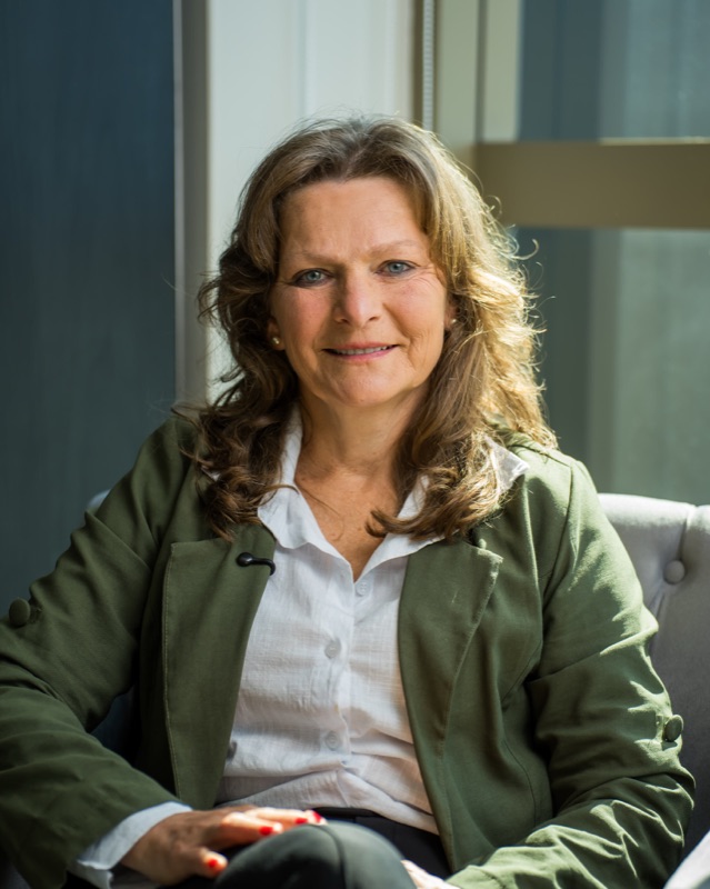 Marcia Bildhauer, terapeuta sistêmica, sorrindo, de casaco verde